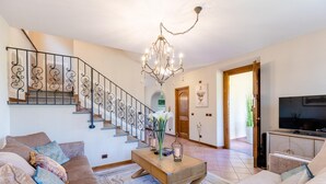 A spacious living room with a staircase, a chandelier, a television, and a sofa set. - Nonna Bianca Farmhouse (Lucca)