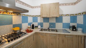 A kitchen with a gas stove, wooden cabinets, a sink, and blue and white tiled backsplash. - Amore Rentals - Casa Barbera B (Positano)
