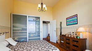 Une chambre à coucher comprenant un lit, une commode, une lampe et une porte-fenêtre coulissante donnant sur un balcon.