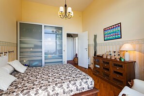 A bedroom with a bed, a dresser, a lamp, and a sliding glass door leading to a balcony. - Villa The Stone on the Sea (Massa Lubrense)