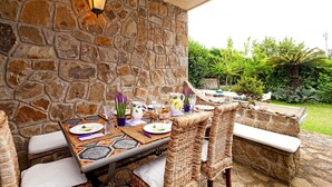 Un espace de restauration en plein air, avec des murs en pierre, des chaises en osier et une table dressée pour un repas.