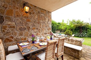 An outdoor dining area with stone walls, wicker chairs, and a table set for a meal. - Villa The Stone on the Sea (Massa Lubrense)