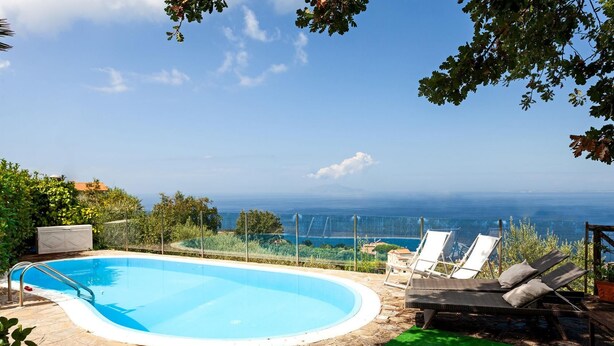 Une piscine avec vue sur l’océan, entourée de chaises longues et d’une pelouse.
