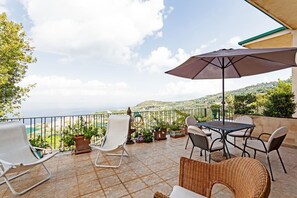 A terrace with a table, chairs, and an umbrella, overlooking a scenic view of the sea and hills. - Villa The Stone on the Sea (Massa Lubrense)