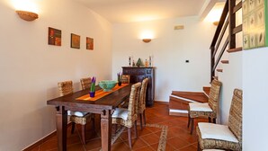 Un coin repas avec une table en bois et des chaises en osier, un meuble contenant des objets décoratifs et un escalier muni d’une rampe.
