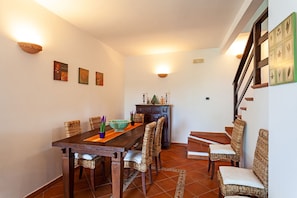 A dining area with a wooden table and wicker chairs, a cabinet with decorative items, and a staircase with a railing.