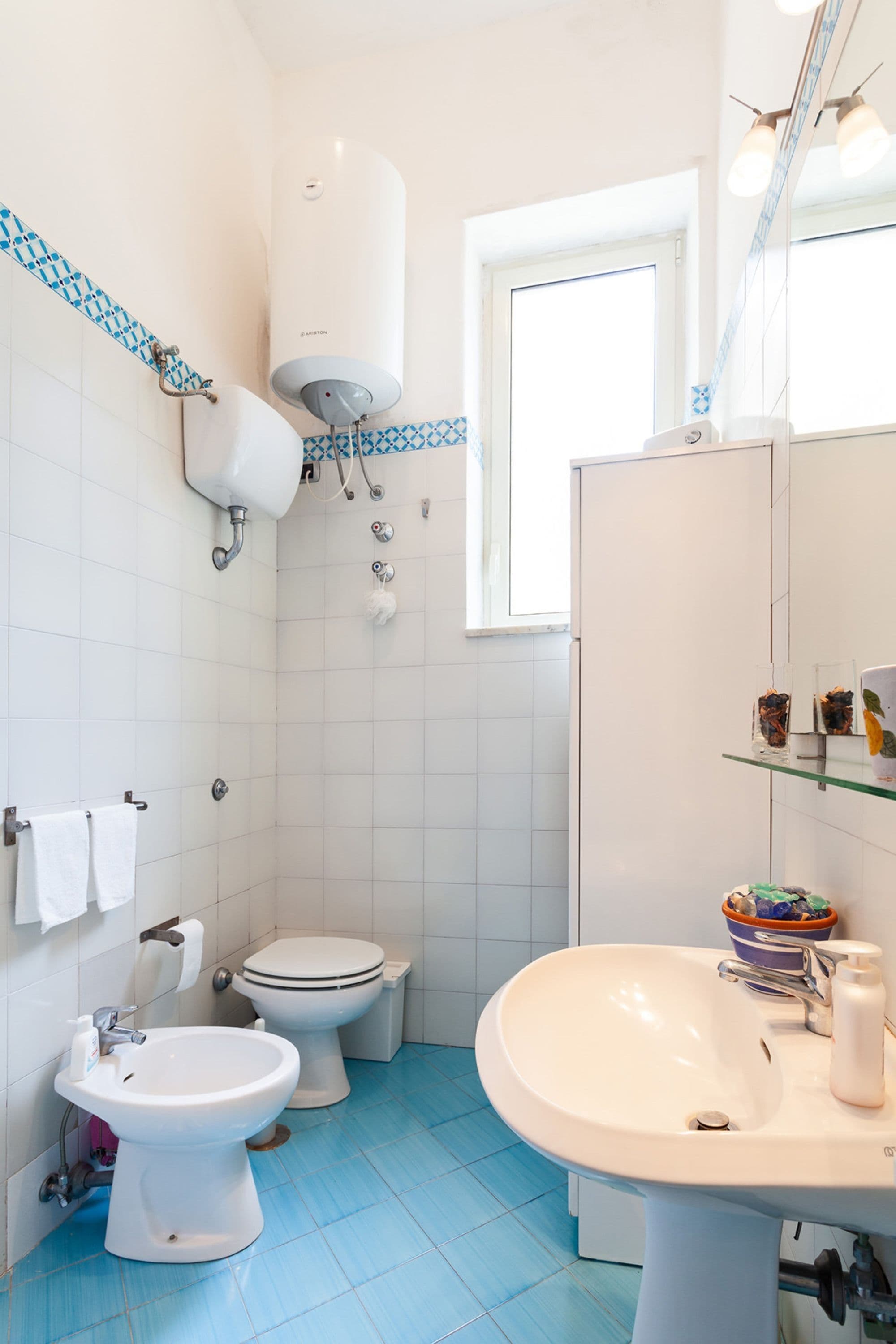 A bathroom with a toilet, bidet, and sink, white tiles, and a window.