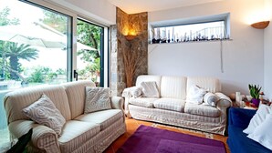 Un salon avec deux canapés, un mur d’accent en pierre, une fenêtre donnant sur un espace verdoyant et une étagère ornée d’objets décoratifs.