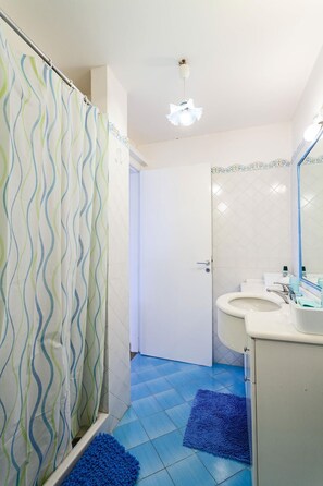 A bathroom with a shower curtain, a sink, a mirror, and a blue rug on the floor. - Villa The Stone on the Sea (Massa Lubrense)