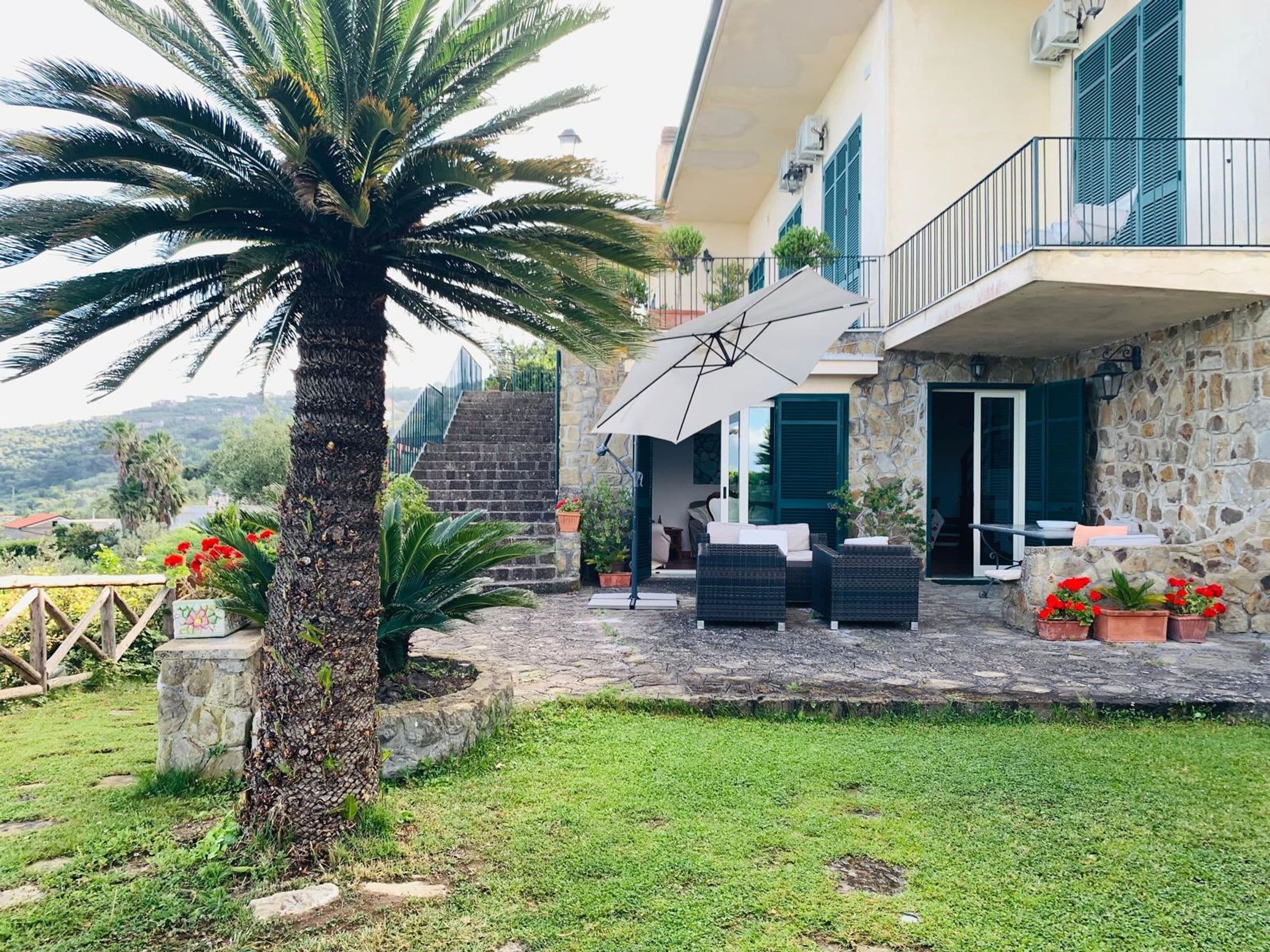 A stone building with a balcony, outdoor seating, and a palm tree.