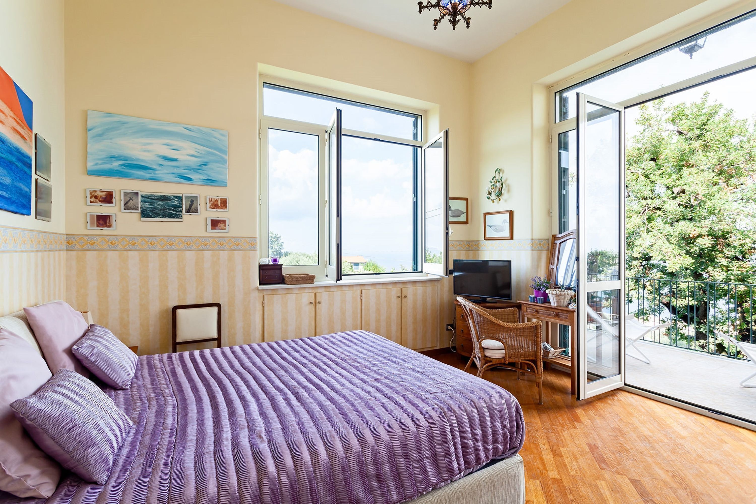 Un dormitorio con una cama grande, un escritorio y un balcón con vistas a zonas verdes.