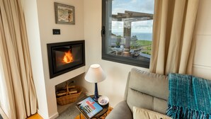 A cozy living room with a fireplace, a comfortable sofa, a table with a book, and a view of the sea through a large window. - Tradicampo-Cycas-Casa da Cisterna- Romantic little corner - NEW LISTING (Algarvia)