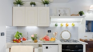 Una cocina con armarios blancos, encimera blanca y salpicadero con un estampado azul y blanco. Hay plantas sobre los armarios, un fregadero, una estufa y un lavavajillas.