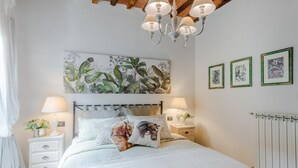 Un dormitorio con cama, mesitas de noche, una lámpara de araña, un radiador y decoración en la pared.