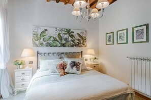 Ein Schlafzimmer mit Bett, Nachttischen, einer Chandelüster, einer Heizung und Wandbildern.