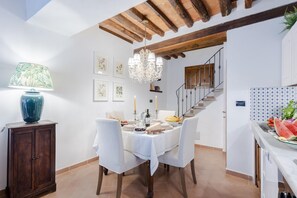 A dining area with a white tablecloth, wooden chairs, a chandelier, and a staircase in the background. - Rio Delle Fate in Vorno (Capannori)