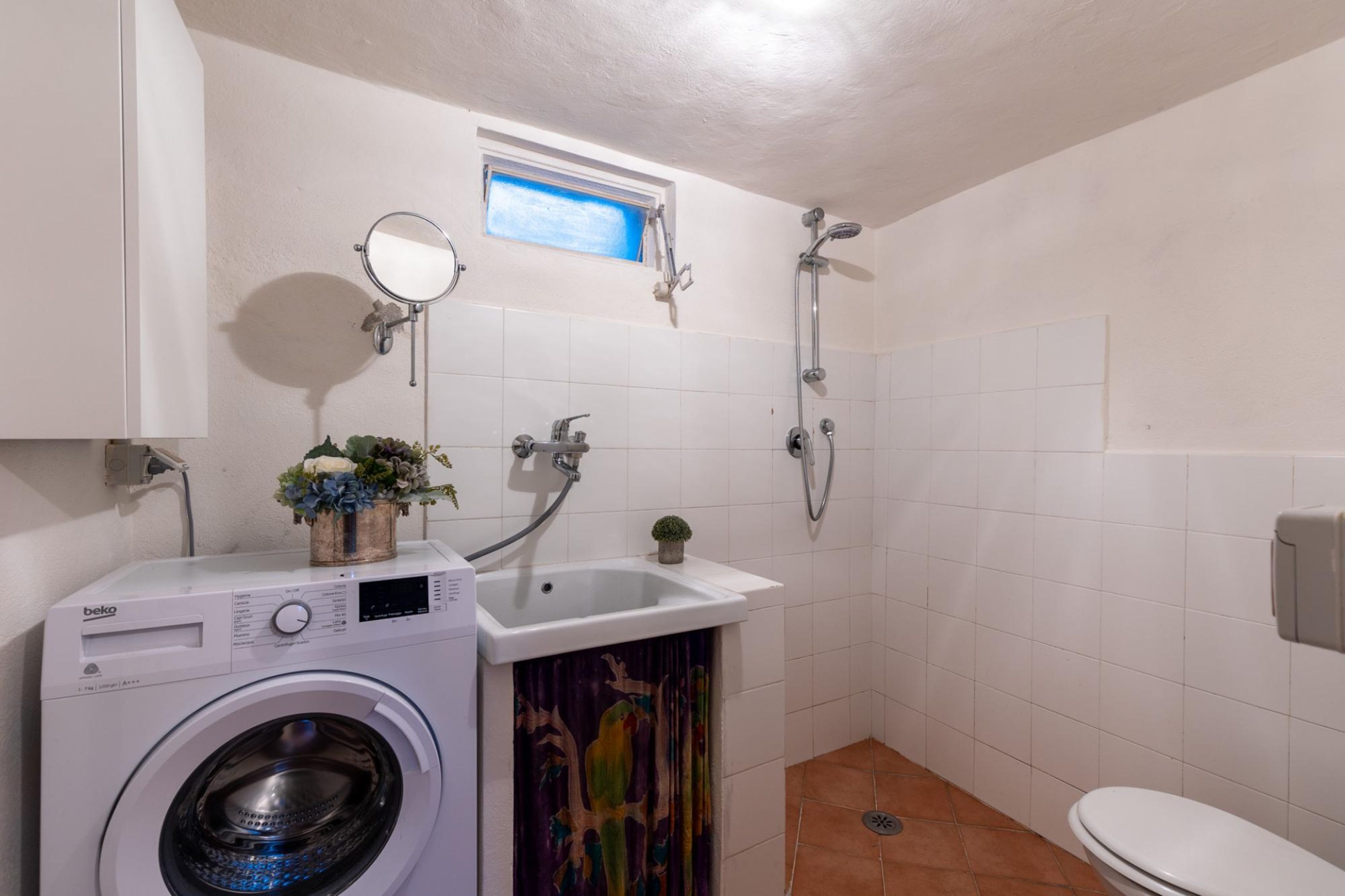 A compact bathroom with a washing machine, a sink, a shower, and a toilet.