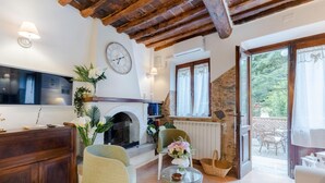 Una sala de estar acogedora con chimenea, vigas de madera, un comedor con mobiliario de exterior y una pared de piedra.