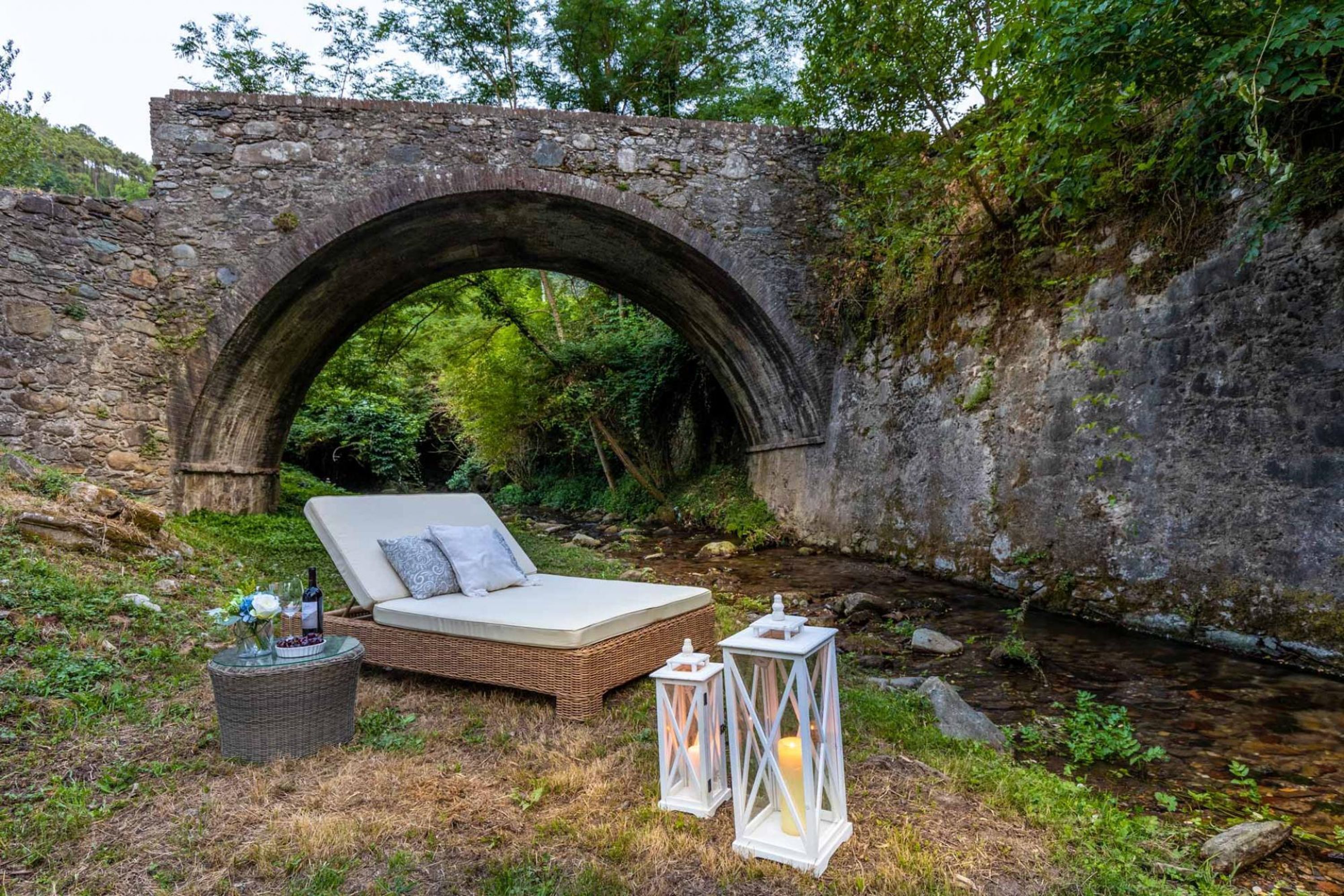Un pont de pierre avec un parterre de fleurs et des lanternes, situé dans une zone boisée.