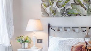 Un dormitorio ordenado con una cama, una mesita de noche con lámpara y una pared decorada con motivos de hojas tropicales.
