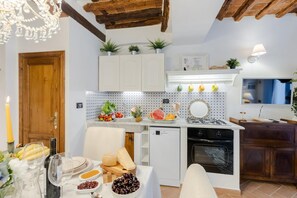 Une cuisine avec des meubles blancs, une cuisinière blanche et un petit réfrigérateur. On y trouve une table à manger avec des assiettes, des verres et une bougie.