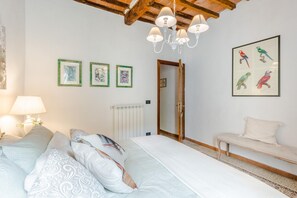 A bedroom with a bed, a bench, a radiator, framed pictures, and a chandelier. - Rio Delle Fate in Vorno (Capannori)