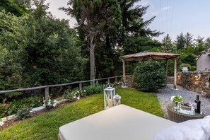 Une terrasse dotée d’un espace salon avec des coussins, d’une pergola et d’un mur en pierre.