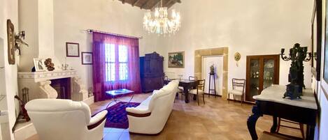 A spacious living room with a high ceiling, a chandelier, a fireplace, and a dining area with chairs and a table.