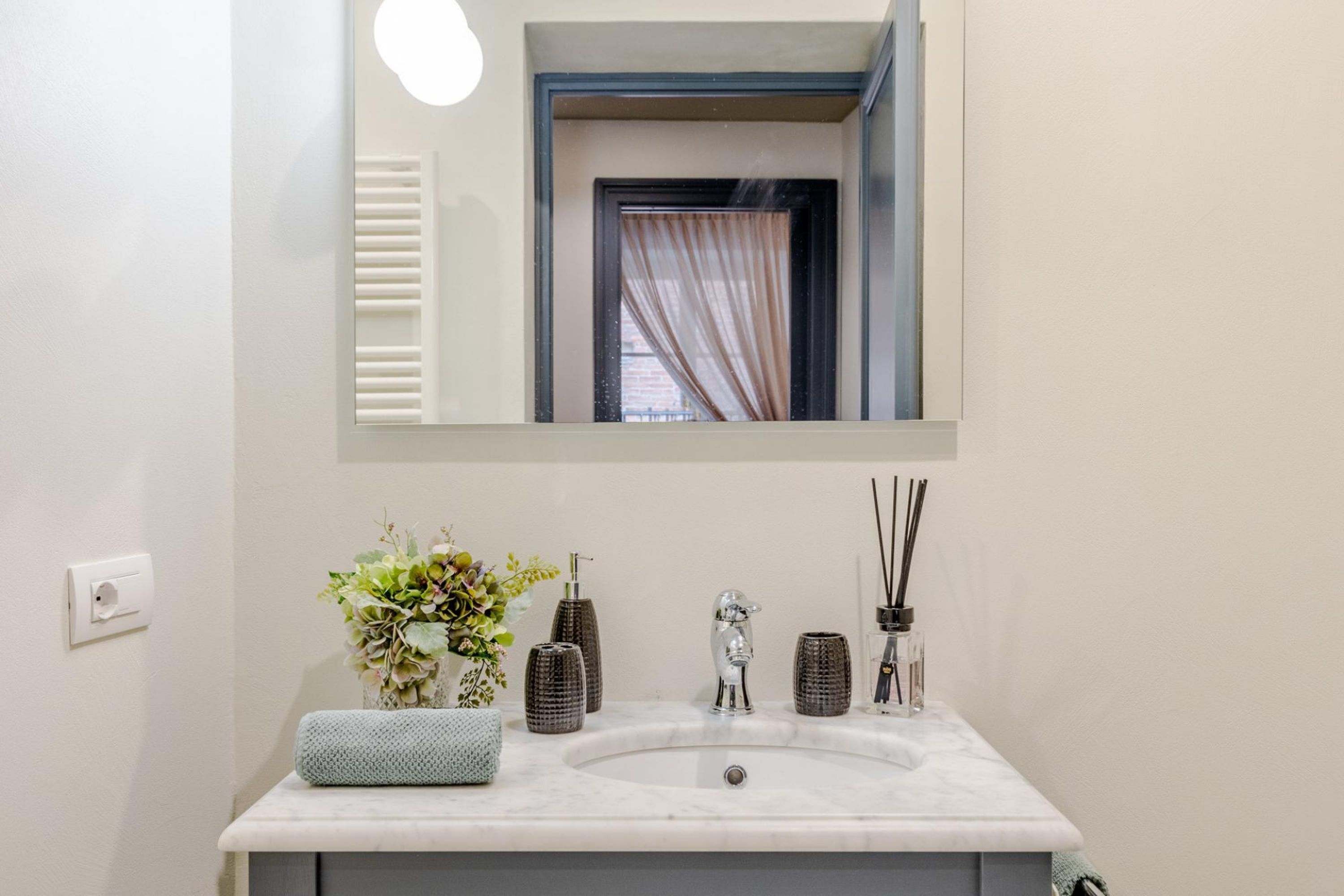 A bathroom with a white sink, a mirror, and a window with curtains.