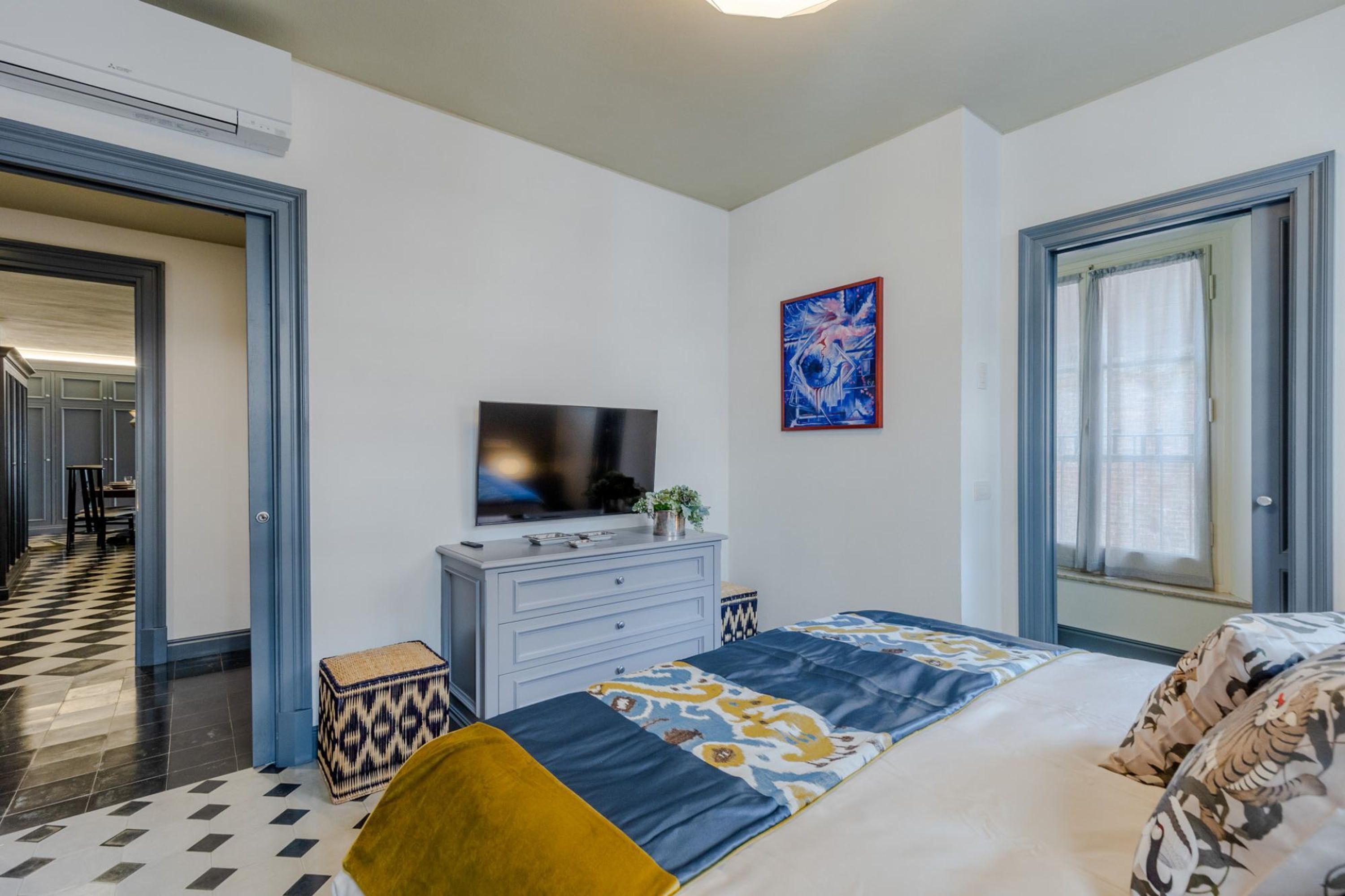 A hotel room with a bed, a television, a painting on the wall, and a window with curtains.