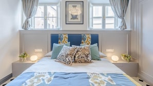 A bedroom with a large bed, two bedside tables with lamps, a framed artwork above the bed, and a window with curtains. - Gimber Tales a First Floor Apartment (Lucca)