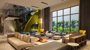 A modern living room with a large sofa, armchairs, a coffee table, and a bookshelf. A staircase with greenery is visible in the background. -  Grand Banyan Hotel  (Tainan)