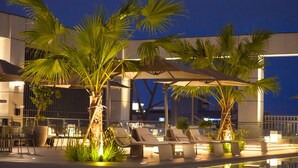 An outdoor pool area with lounge chairs and palm trees, surrounded by a modern building. -  Grand Banyan Hotel  (Tainan)