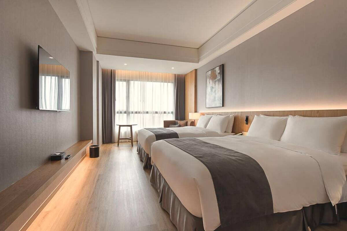 A modern hotel room with a large bed, bedside tables, a flat-screen TV, and a view of the city.