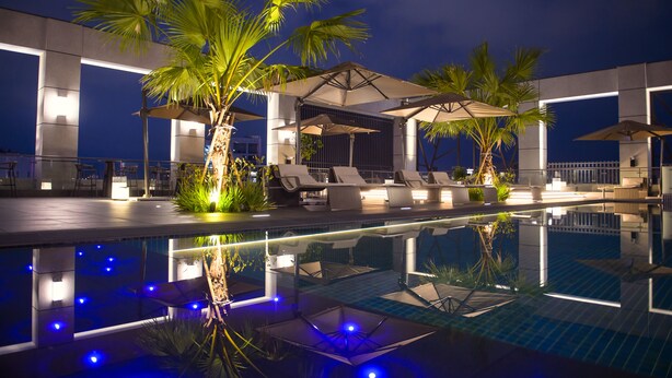 A nighttime pool area with lounge chairs and umbrellas, surrounded by palm trees and modern architecture. -  Grand Banyan Hotel  (Tainan)