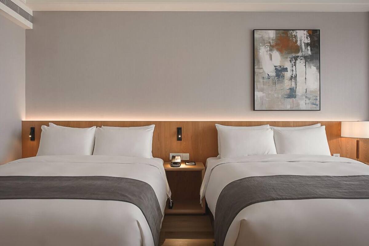 A hotel room with two beds, a nightstand with a lamp, and a painting on the wall.
