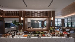 A buffet setup with various food items and condiments, a marble countertop, and a modern interior design with wooden accents and large windows. -  Grand Banyan Hotel  (Tainan)