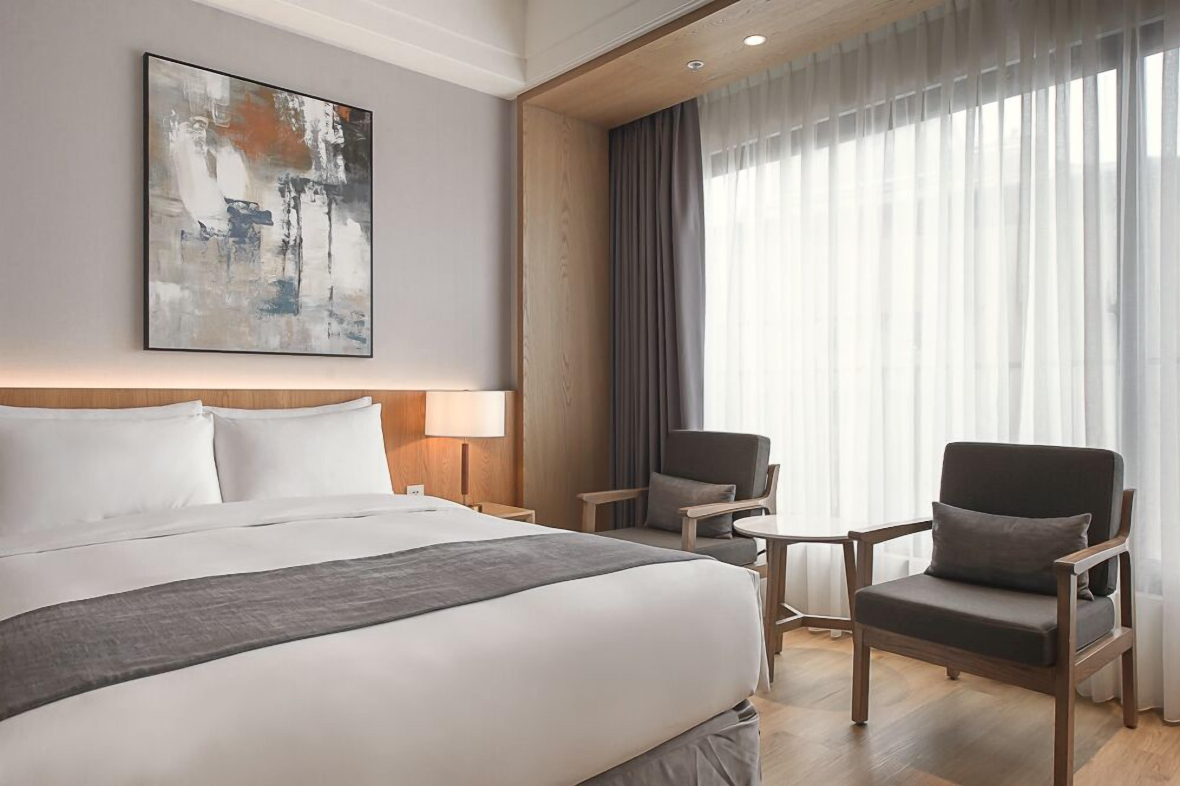 A hotel room with a large bed, two armchairs, a small table, and a painting on the wall.
