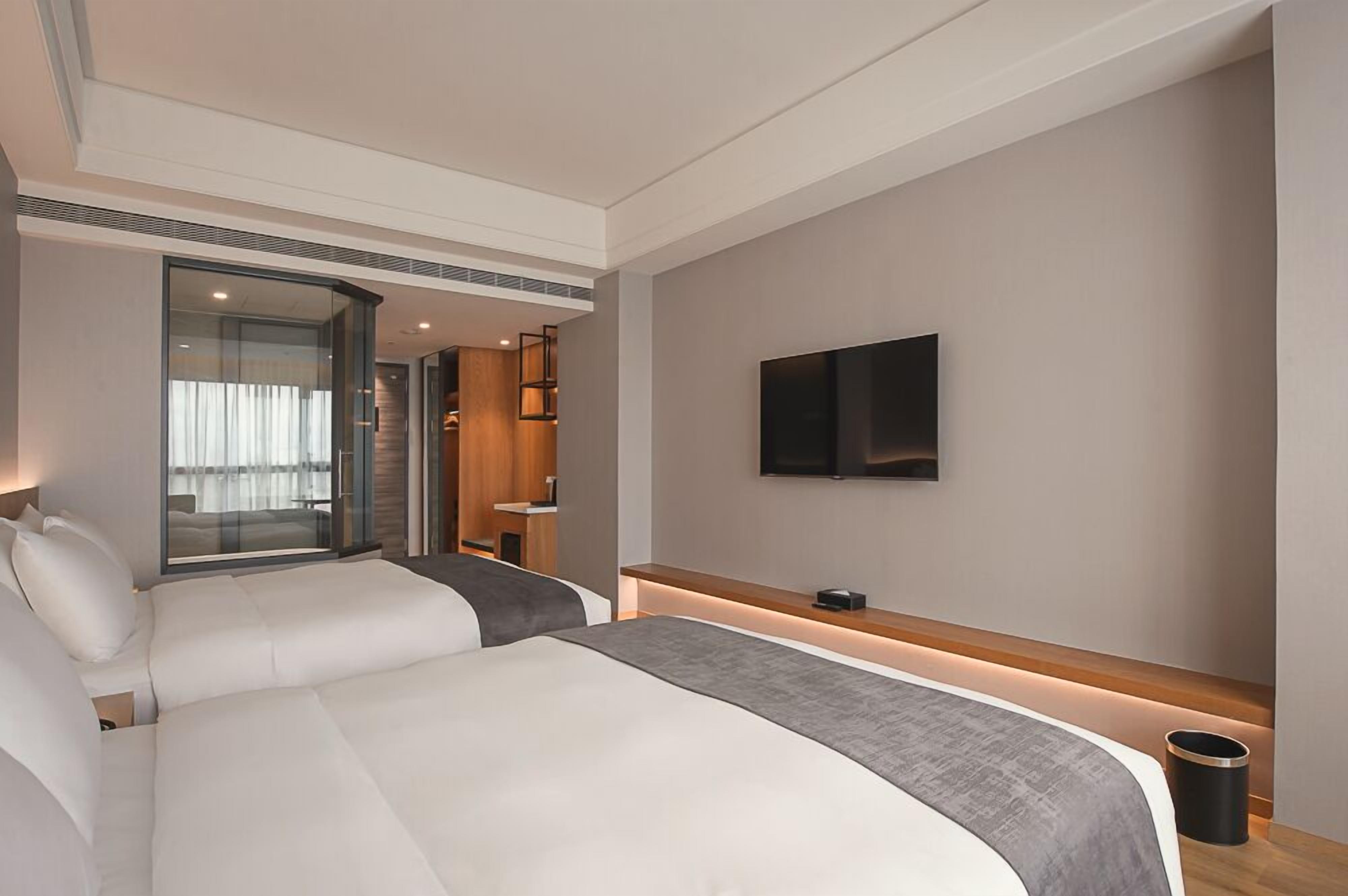 Una habitación de hotel moderna con dos camas, un televisor y un puerta de cristal que da a un balcón.