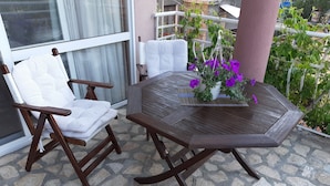 Een houten stoel en tafel staan op een terras van natuursteen, met een bloempot met paarse bloemen.
