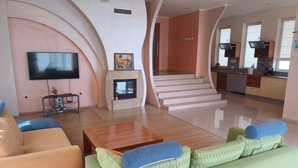 Een moderne woonkamer met een bank, een salontafel, een open haard, een televisie en een keukenhoek met een trap.