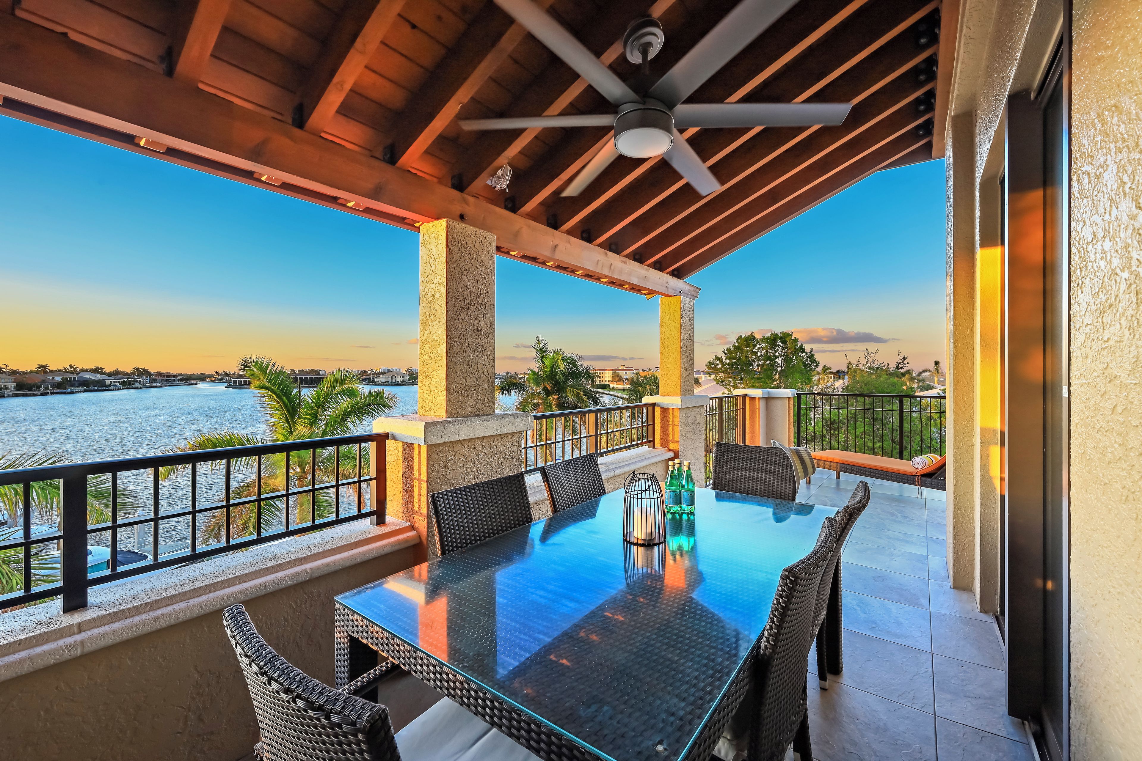 A covered outdoor patio with a glass table, chairs, and a view of a body of water.