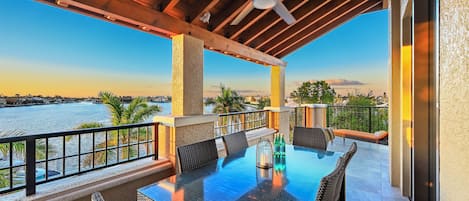 A covered outdoor patio with a glass table, chairs, and a view of a body of water.