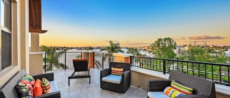 A balcony with wicker furniture, a view of the city, and a clear sky.