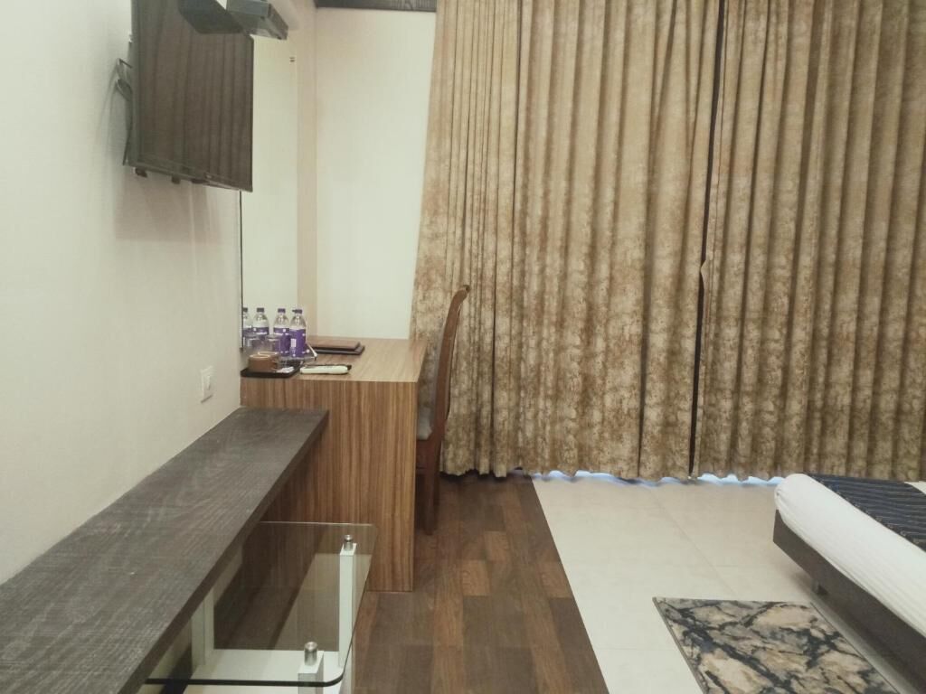 Una habitación compacta con escritorio de madera, un mueble pequeño, un sofá y una ventana con cortinas.