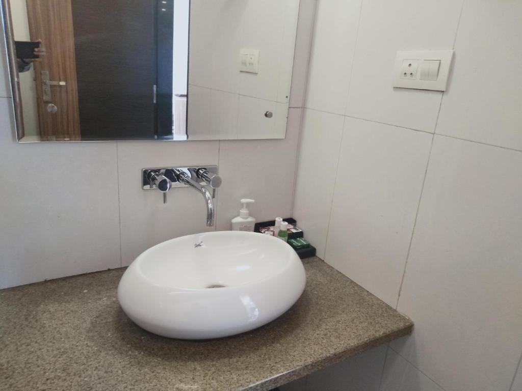 A bathroom with a round white sink, a mirror, and a faucet. There are toiletries on the countertop.