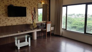 Une chambre moderne dotée d’une grande fenêtre, d’un téléviseur à écran plat fixé au mur, d’un bureau en bois et d’une table basse en verre.