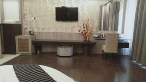 Une chambre d’hôtel comprenant un lit, un bureau, une chaise, un téléviseur fixé au mur et un vase décoratif avec des fleurs.