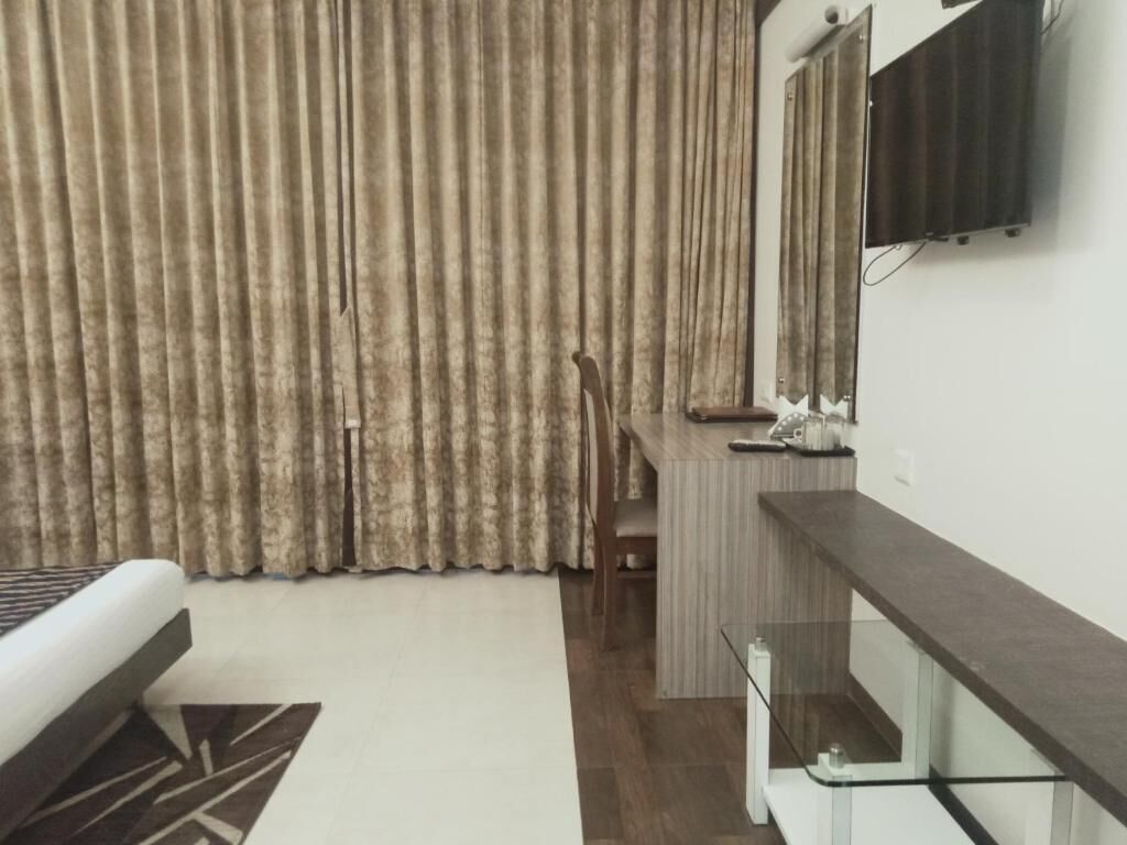 A hotel room with a bed, a desk, a chair, a TV, and a window with curtains.