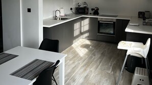 A modern kitchen with a white countertop, black appliances, and a dining area with a white table and black chairs. - 1892 Schoolhouse Killarney - ideal for Ring of Kerry, Dingle & Killarney (Killarney)